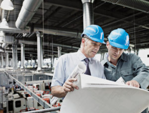 Businessmen looking at blueprints in factory